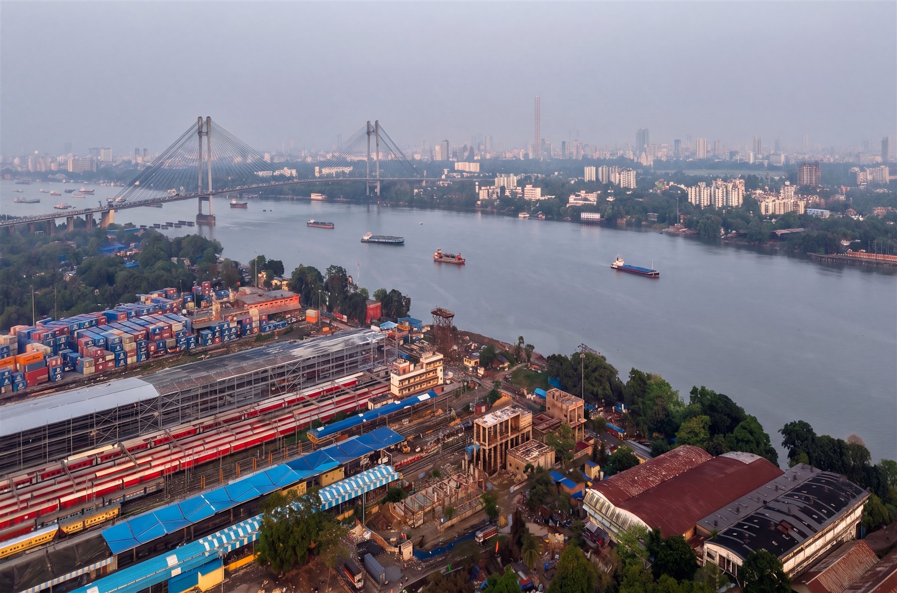 Shalimar Station from the air — platforms, rakes and the new trainshed under construction, with Vidyasagar Setu and the Kolkata skyline beyond